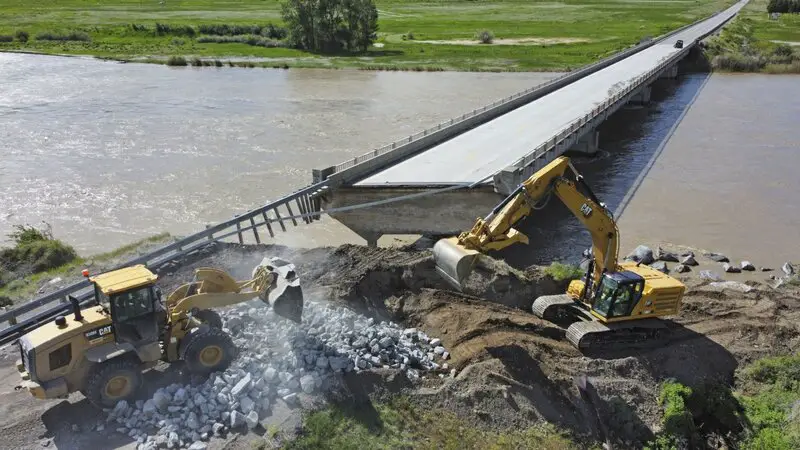 Highway workers build up the shoreline of a washed out bridge along the Yellowstone River Wednesday, June 15, 2022, near Gardiner, Mont. Yellowstone National Park officials say more than 10,000 visitors have been ordered out of the nation's oldest national park after unprecedented flooding tore through its northern half, washing out bridges and roads and sweeping an employee bunkhouse miles downstream.